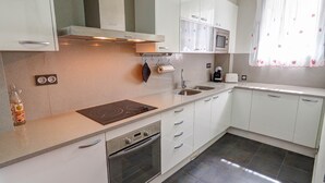 Une cuisine moderne avec des meubles blancs, un four encastré, un four à micro-ondes et une cuisinière à gaz.