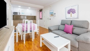 A modern living room with a grey sofa, a white coffee table, and a dining area with a pink tablecloth. - A&n La Cueva 1 . (Torre del Mar)