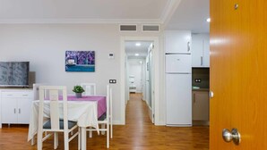 A modern kitchen with white cabinets and a refrigerator, a dining area with a table and chairs, and a hallway leading to another room. - A&n La Cueva 1 . (Torre del Mar)