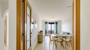 A modern dining area with a wooden table and chairs, a small side table with a plant, and a view through a window with curtains. - A&N La Vega 6, (Torre del Mar)
