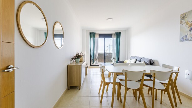 A dining area with a round table and wooden chairs, a wooden cabinet, and two wall-mounted mirrors. - A&N La Vega 6, (Torre del Mar)
