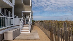 A beachfront property with a wooden deck, a staircase leading to a balcony, and a sandy path. - Silver Sands 102S Direct Ocean Front, Just steps to the Beach! (Ocean City)