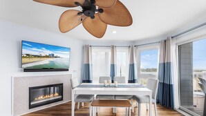 A modern living room with a fireplace, dining table, and large windows. - Silver Sands 102S Direct Ocean Front, Just steps to the Beach! (Ocean City)