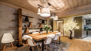 A dining area with a wooden table, white chairs with fur trim, and a chandelier. There are shelves and a vase with flowers on the wall. - PADOUK- Apartment w/ hot tub in Courchevel Moriond (Courchevel)