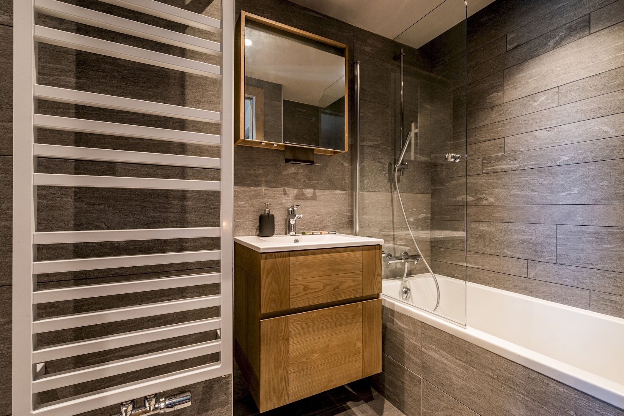A modern bathroom with a wooden vanity, a large mirror, and a glass-enclosed shower.