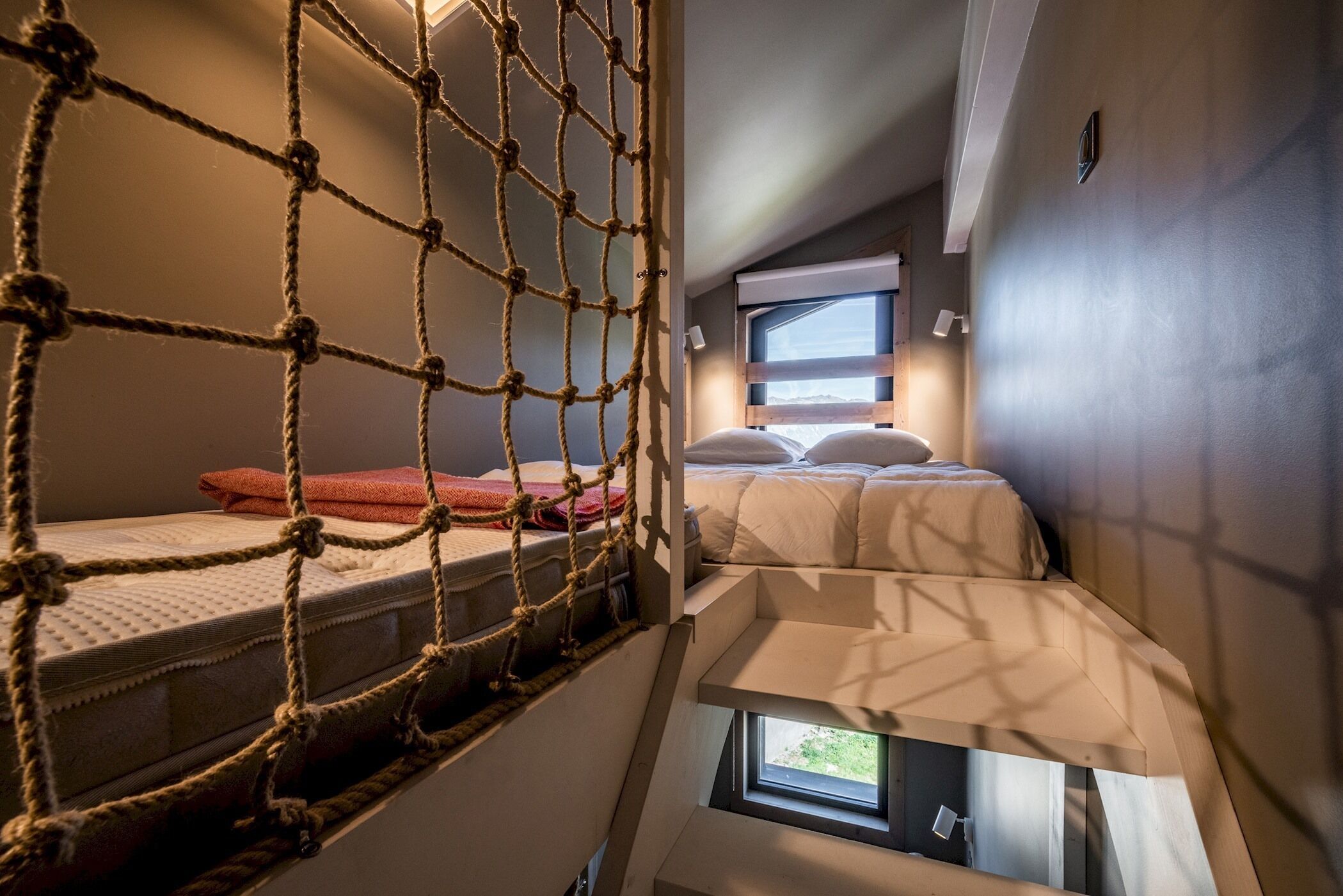 Quarto de hotel pequeno com beliches, uma rede e uma janela.