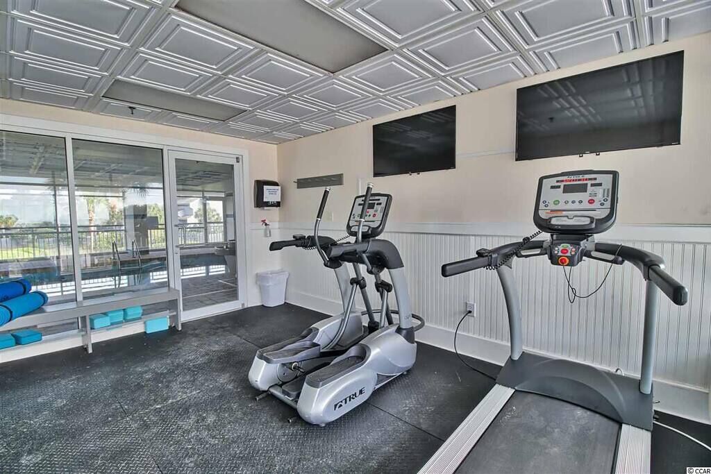 A gym with two treadmills, a wall-mounted TV, and a glass door leading outside.