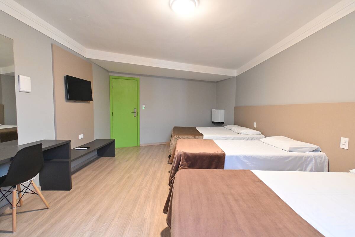 A hotel room with a desk, two beds, a green door, and a television.