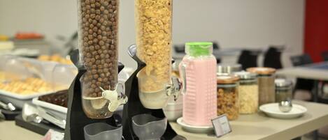 A buffet table with various food dispensers, including a cereal dispenser and a container with a pink lid.