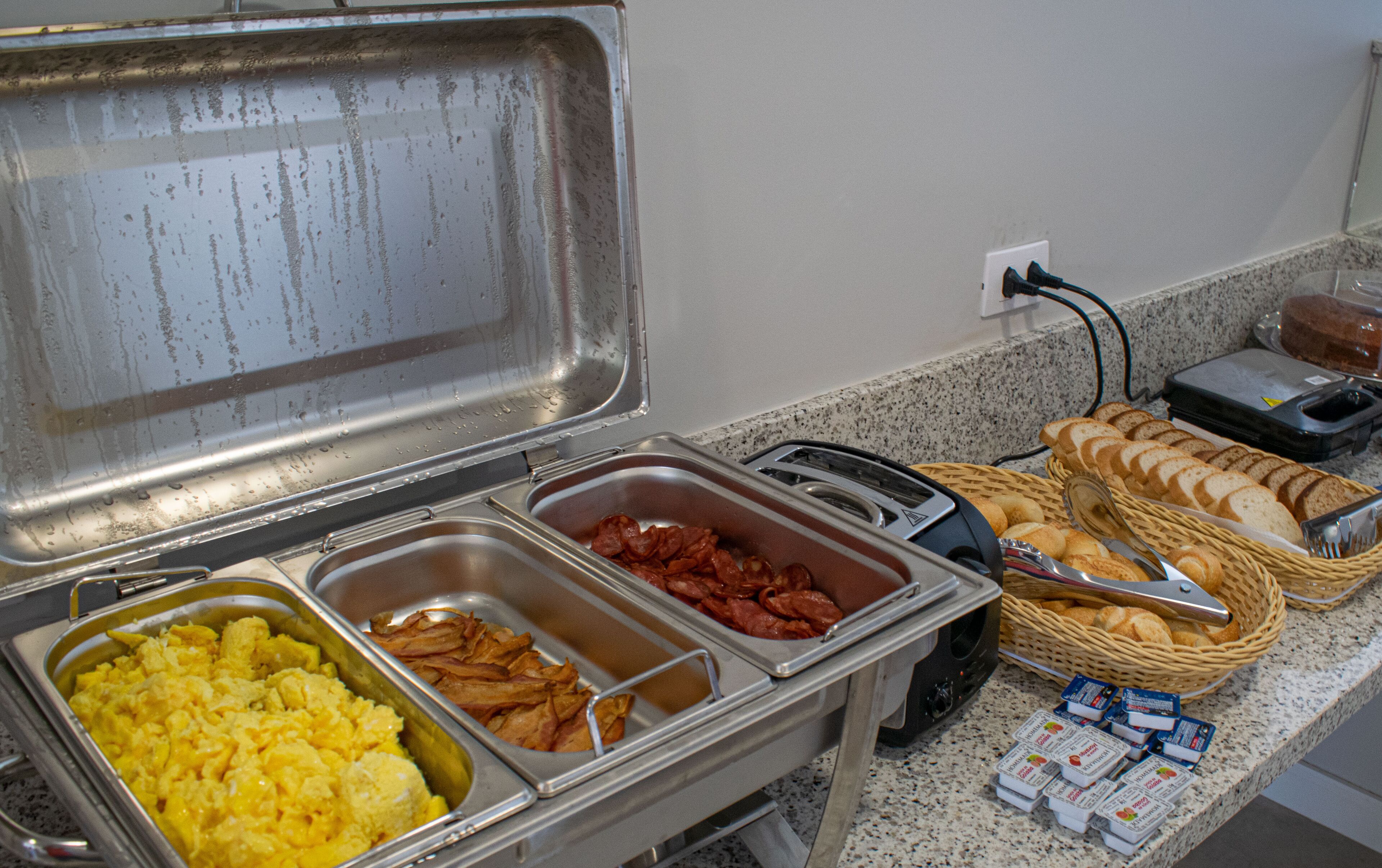 Buffetissa on tarjolla monenlaista ruokaa, kuten munakokkelia, pekonia ja leipää.