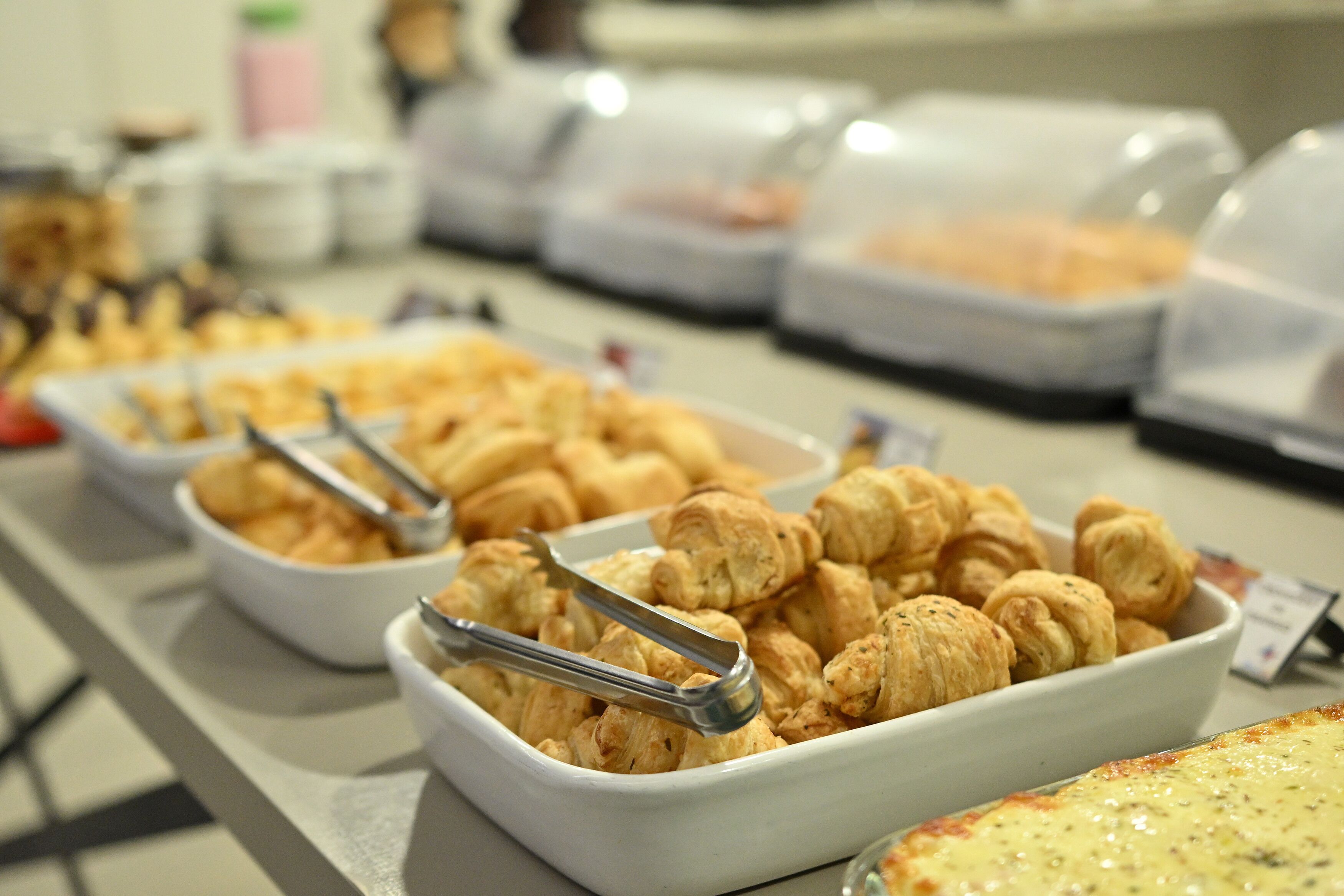 Buffet com diversos alimentos, incluindo doces e um prato grande de massa.