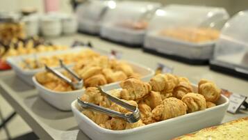Buffet com diversos alimentos, incluindo doces e um prato grande de massa.