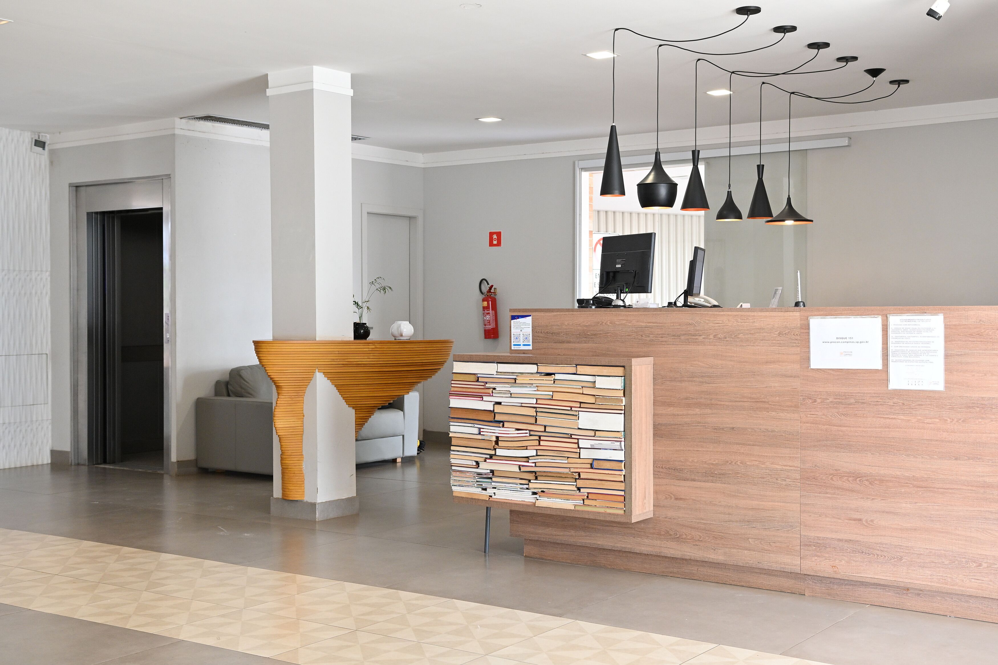 A reception area with a wooden reception desk, a modern pendant light fixture, and a fire extinguisher on the wall.