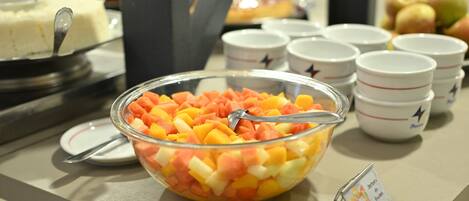 A buffet table with a bowl of mixed fruit, white cups with star designs, and a cake on a stand.