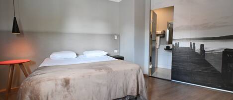 Un dormitorio moderno con una cama grande, un taburete rojo, una lámpara colgante negra y vistas a un muelle a través de una puerta de cristal.