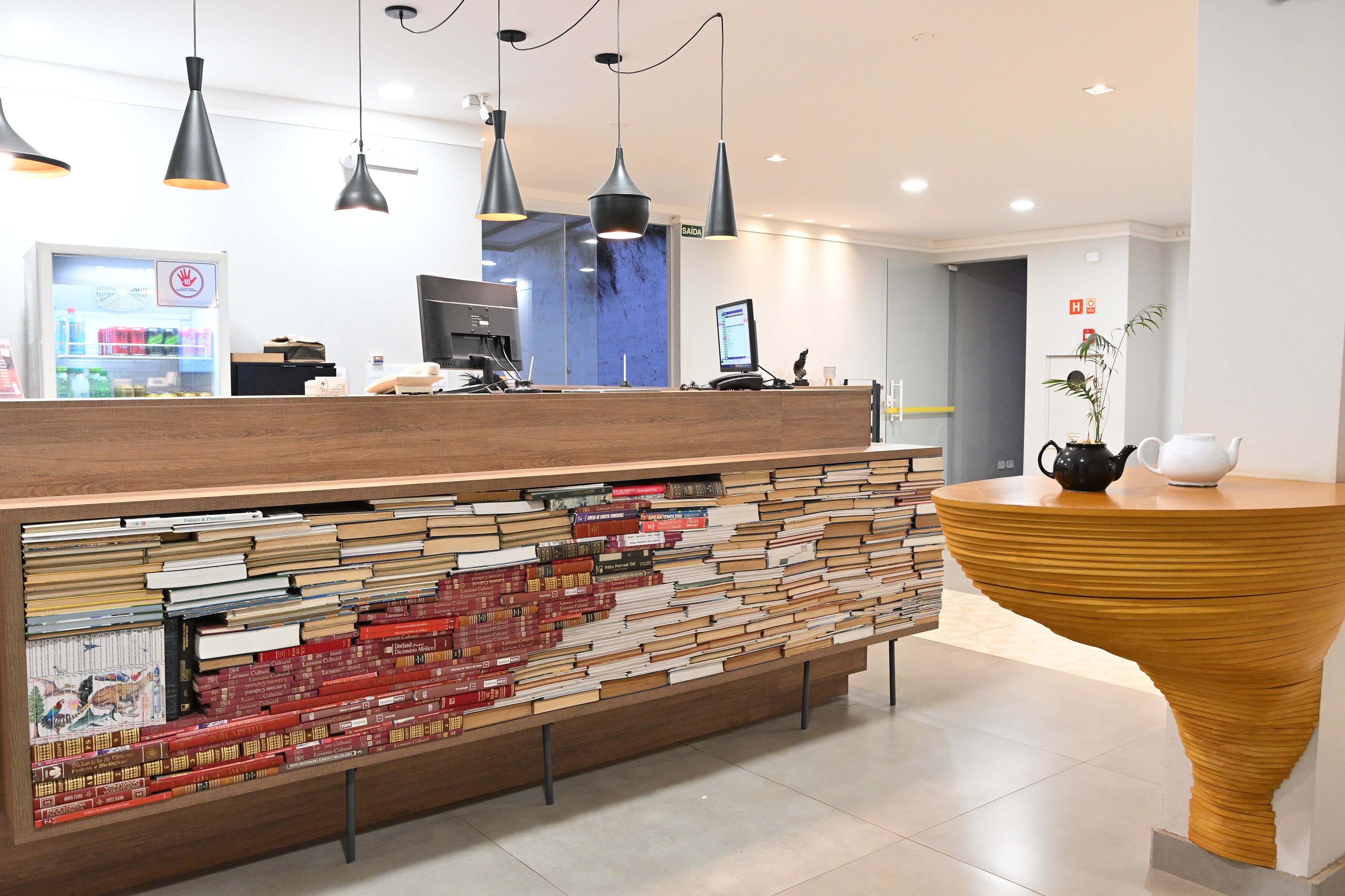 Una recepción con detalles de madera, una estantería llena de libros y un diseño moderno con iluminación colgante.