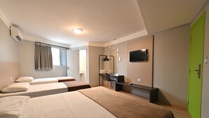Habitación de hotel con tres camas, un escritorio, un espejo, un televisor y una puerta verde.