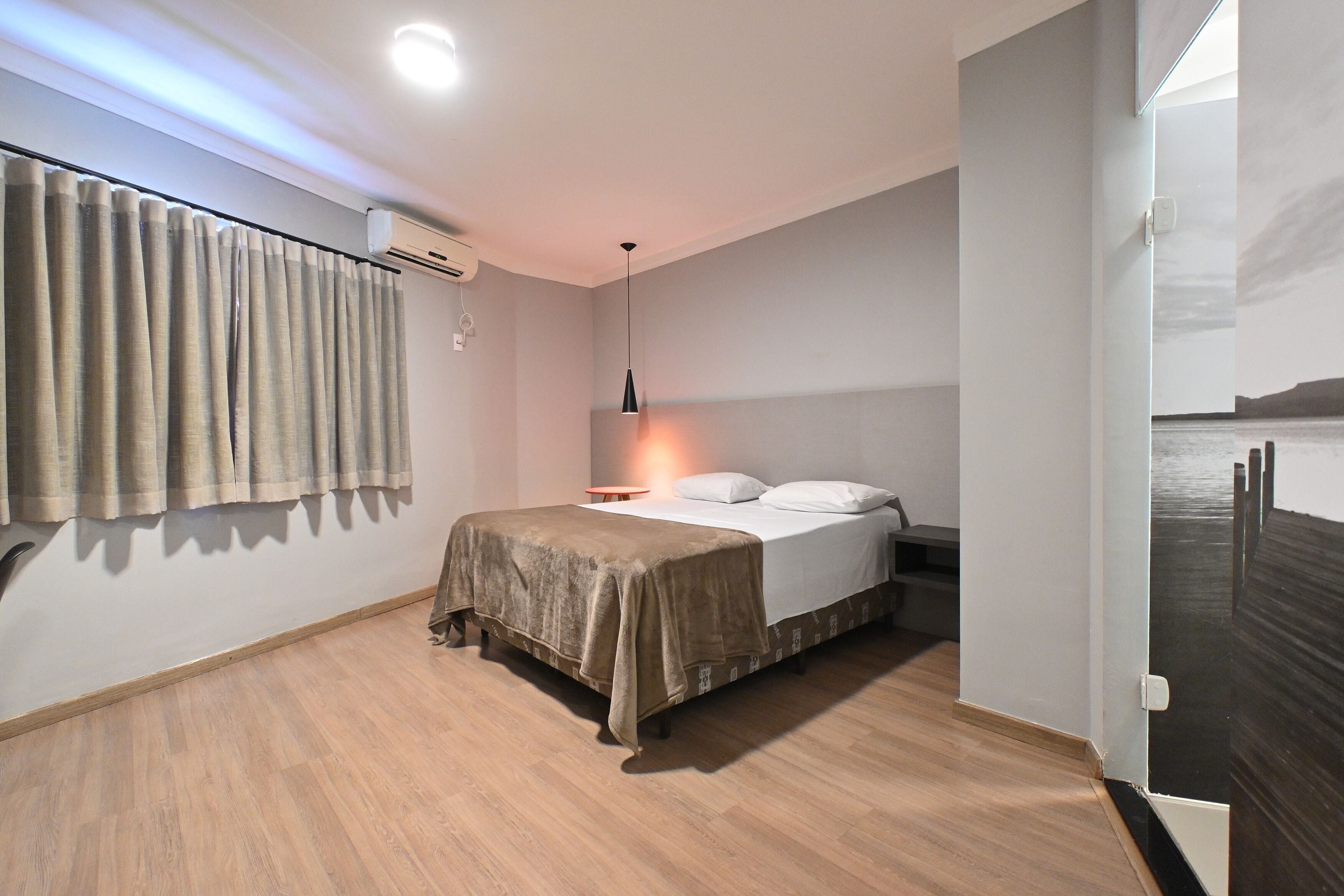 A bedroom with a bed, a bedside table, a lamp, and a window with curtains.