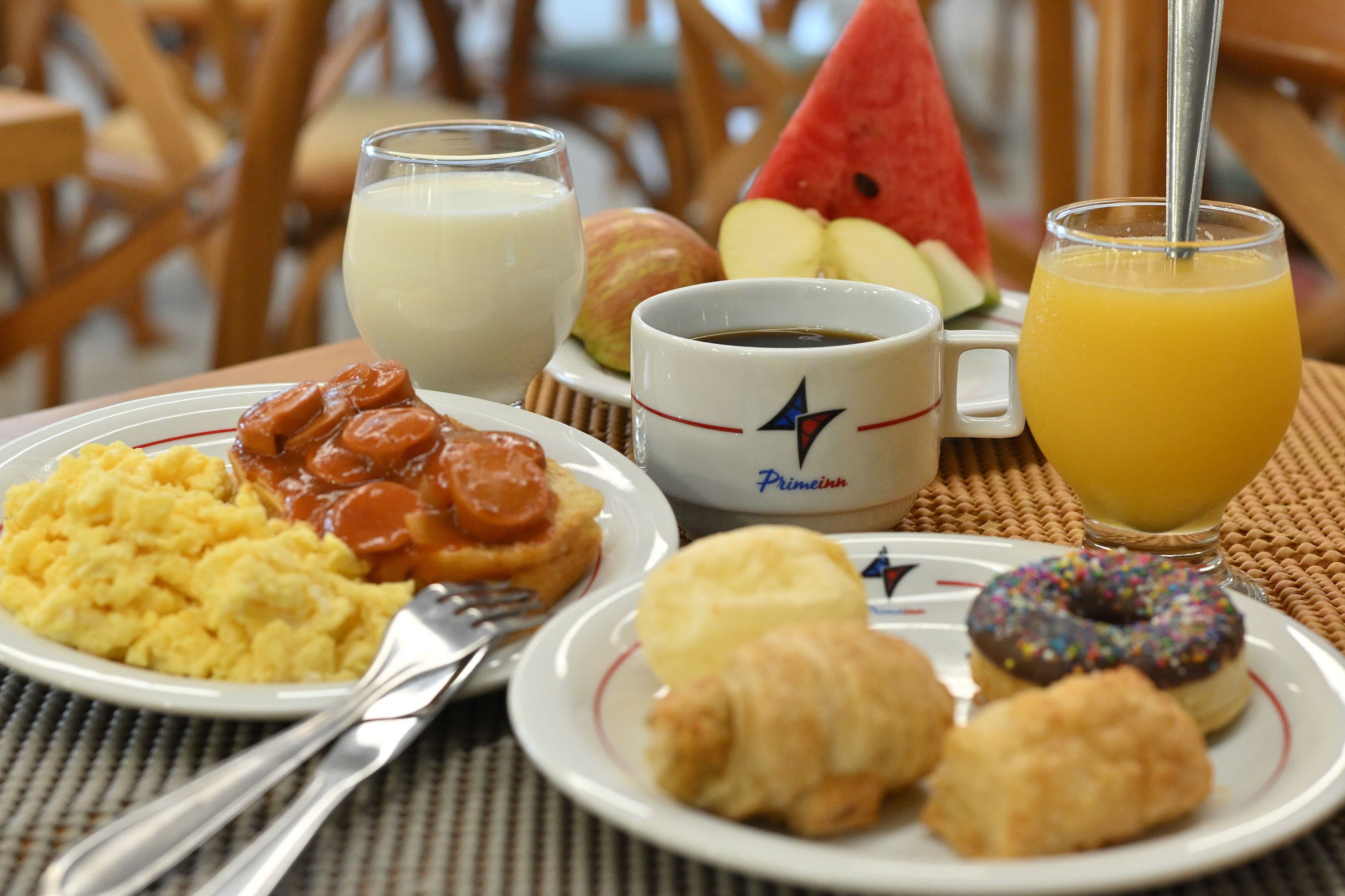 A breakfast setting with plates of scrambled eggs, sausage, croissants, and a muffin, along with a glass of orange juice and a cup of coffee.