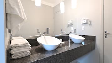 Um banheiro moderno com duas pias, uma pilha de toalhas e um secador de cabelo na parede.