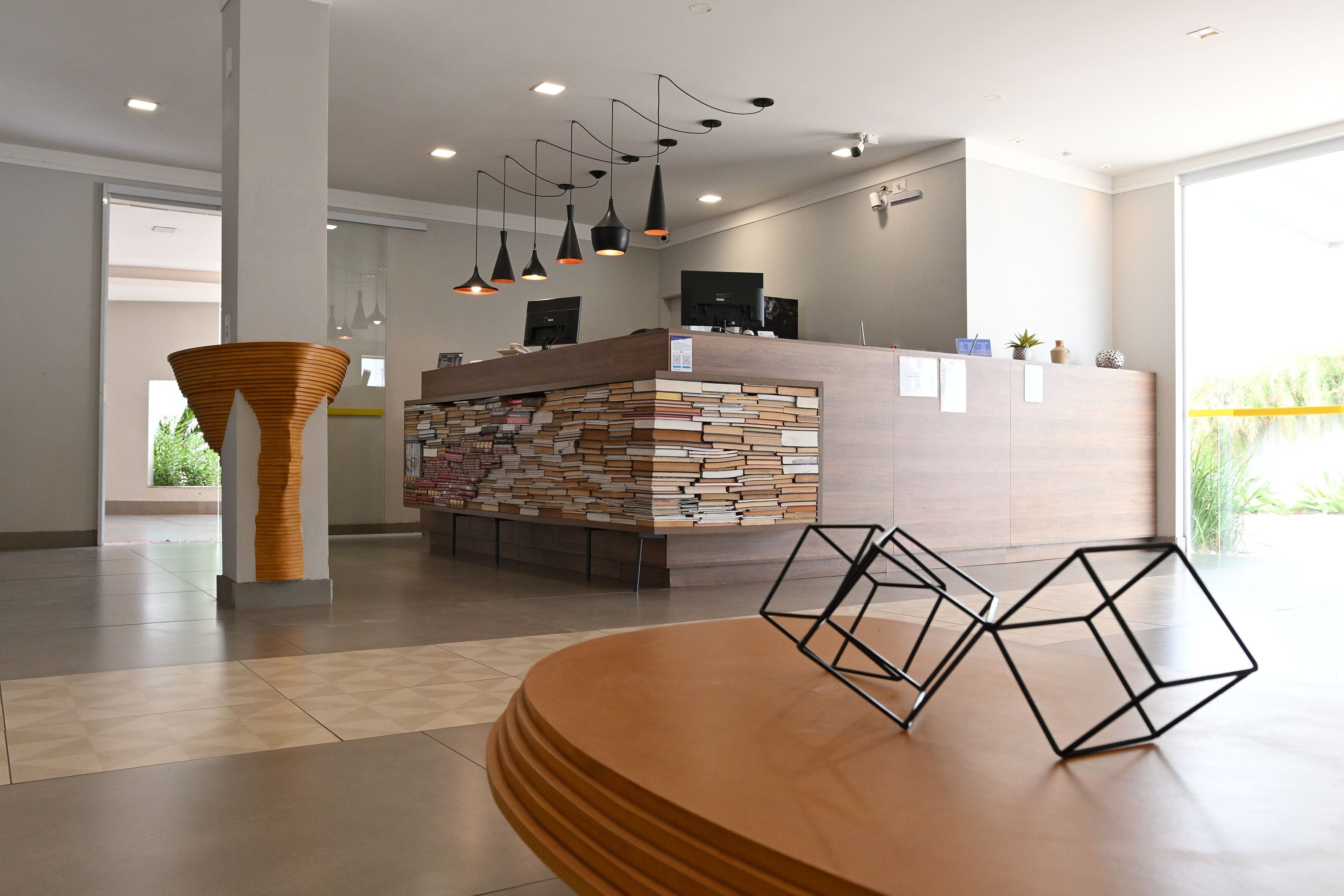 A modern reception area with a wooden reception desk, a stack of books, and geometric metal sculptures.