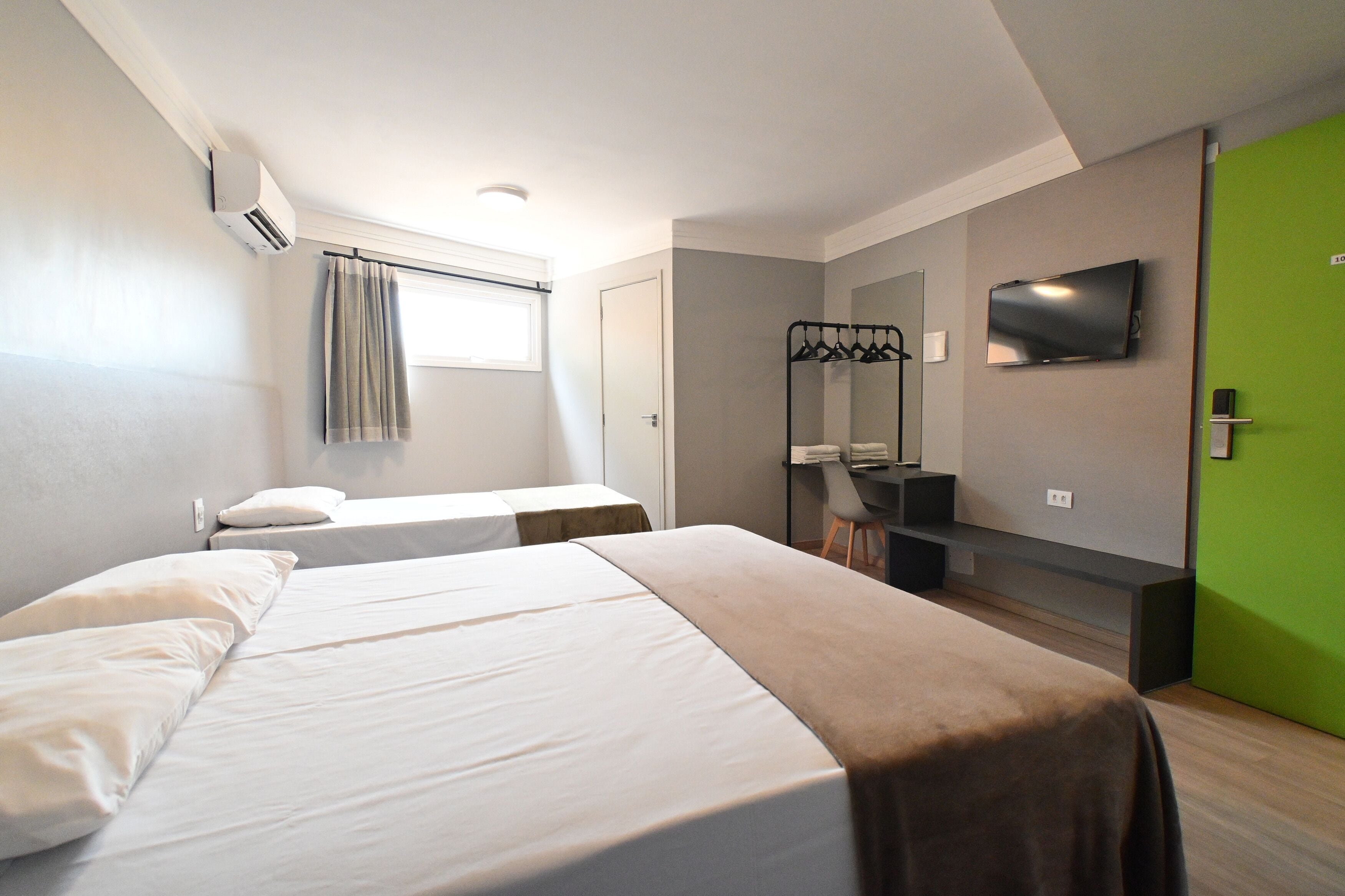 A modern hotel room with a large bed, a TV mounted on the wall, and a green door.