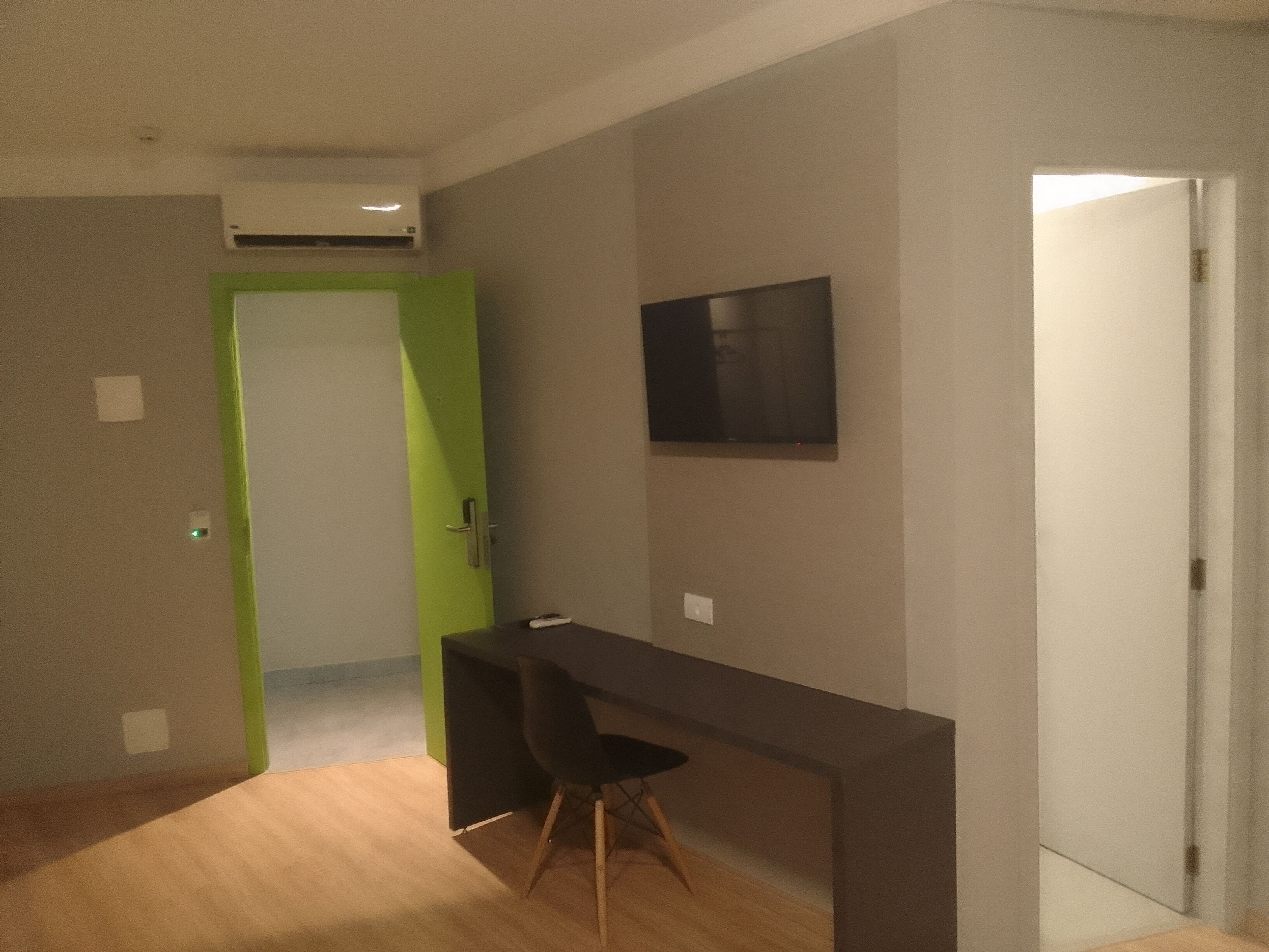 A room with a desk, chair, and a flat-screen TV mounted on the wall.