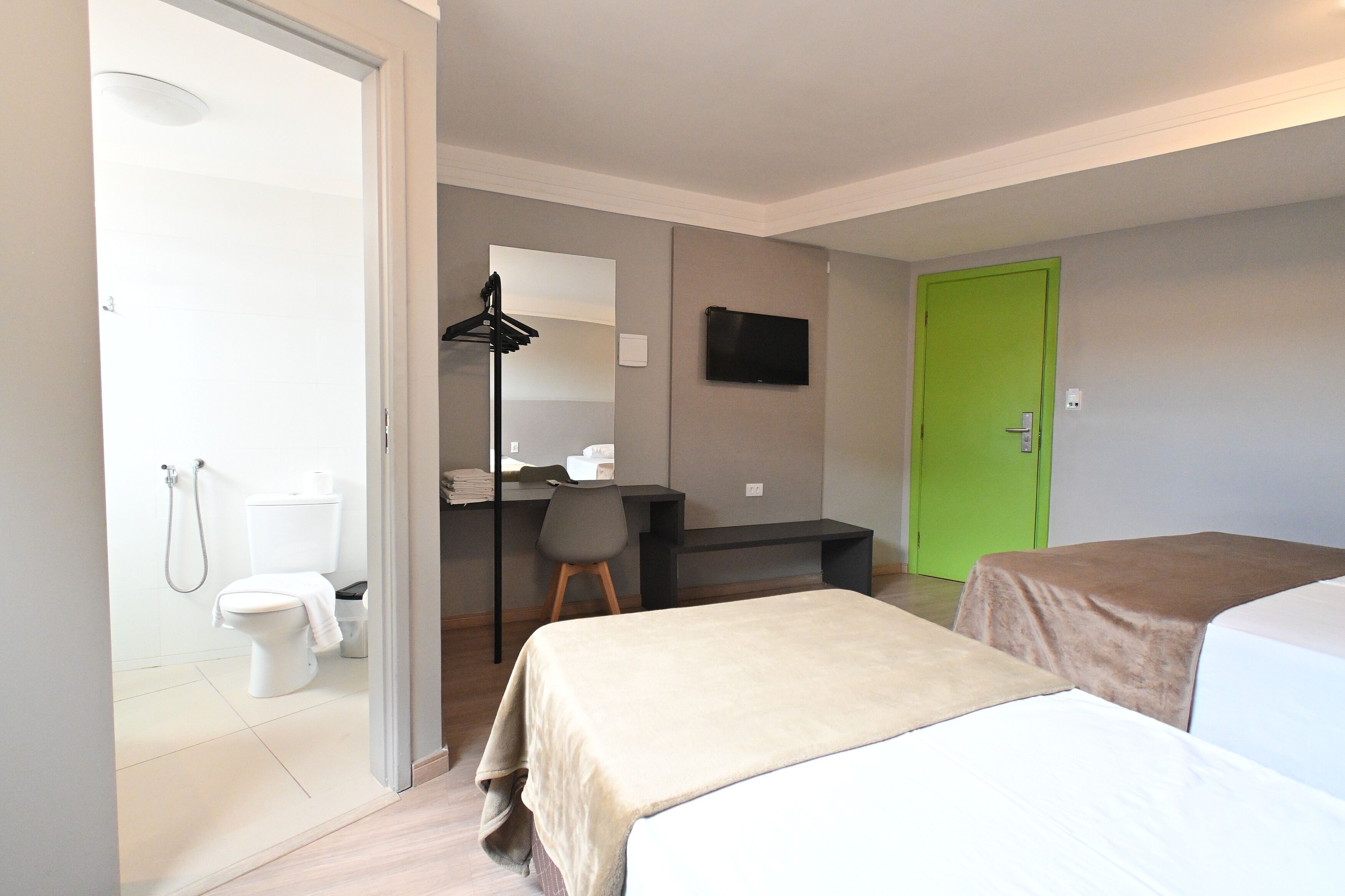 Habitación de hotel con cama, escritorio con silla, puerta verde y baño con inodoro y ducha.