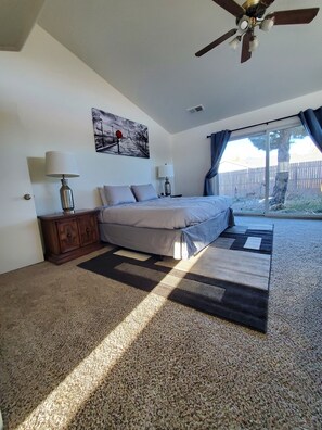 Cozy retreat with a large bed, ceiling fan, and artwork, set against a carpeted floor with a patterned rug.