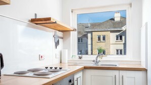 Una cocina moderna con armarios blancos, encimera de madera, horno empotrado y ventana con vistas a un edificio residencial.