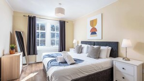 Un dormitorio ordenado con cama, mesitas de noche, una ventana con cortinas y una obra de arte colgada en la pared.