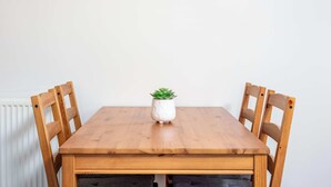 Una mesa de comedor de madera con cuatro sillas, un jarrón blanco con una planta verde y un radiador blanco al fondo.