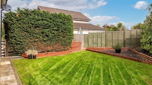 A well-maintained backyard with a neatly trimmed lawn, a wooden fence, and a large hedge.