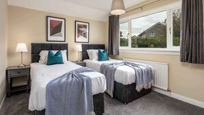 A hotel room with two beds, a window with curtains, a radiator, and artwork on the wall. - Leeward House - Donnini Apartments (Ayr)