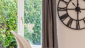 A room with a window, a chair, a table, and a wall clock. - Leeward House - Donnini Apartments (Ayr)