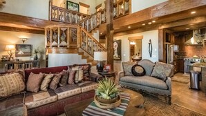 A spacious living area with a large wooden staircase, a fireplace, and a kitchen area visible through an open door. - Unique mountain home with hot tub (Angel Fire)