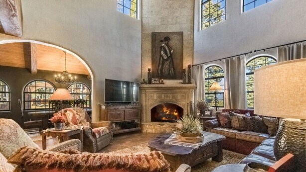 A spacious living room with a fireplace, comfortable seating, and large windows. - Unique mountain home with hot tub (Angel Fire)