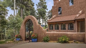 A rustic building with a large arched entrance, surrounded by greenery and trees. - Unique mountain home with hot tub (Angel Fire)