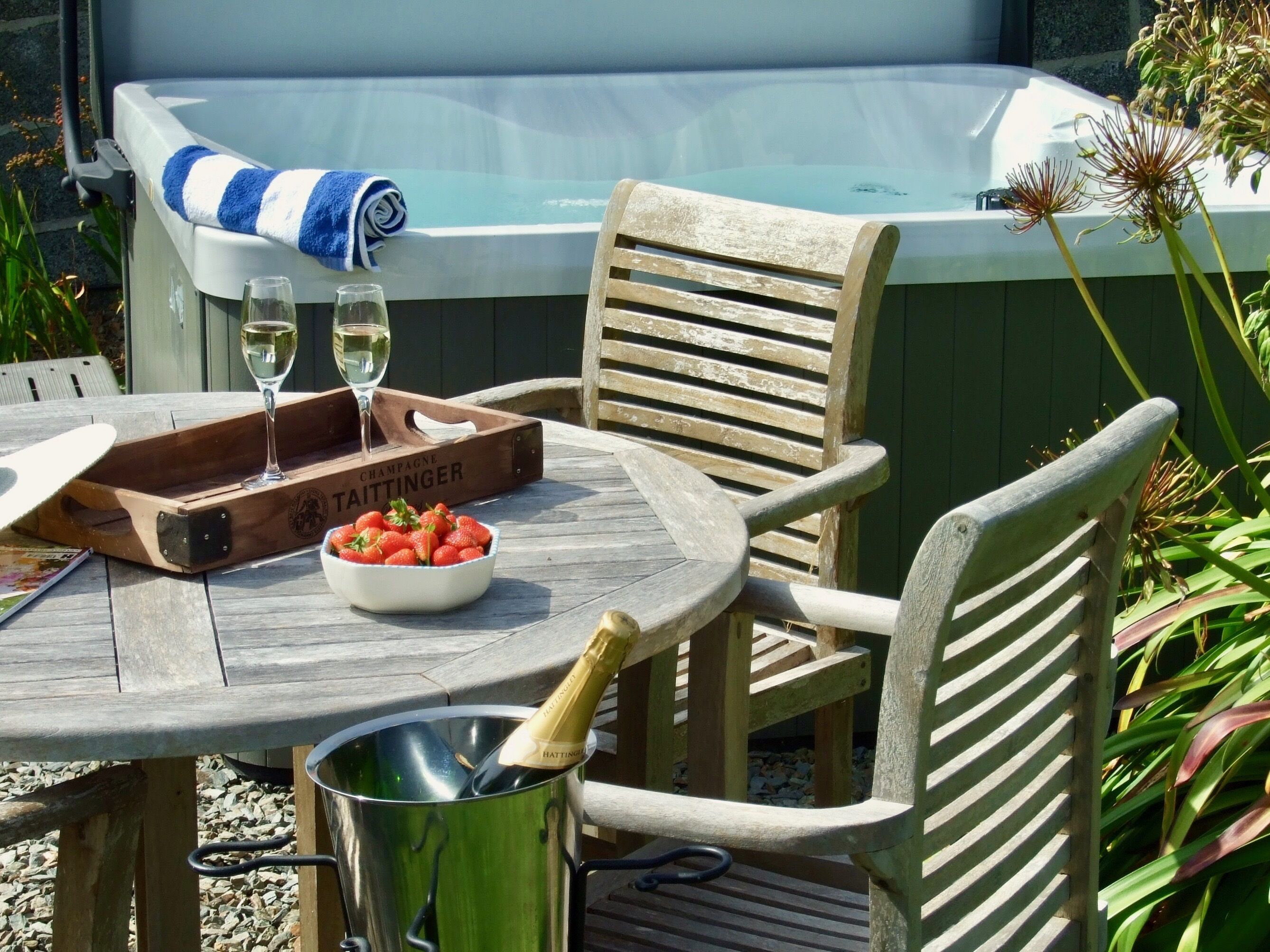 A wooden table with a bowl of strawberries, a bottle of champagne, and a glass of wine. A wooden chair is positioned next to the table.
