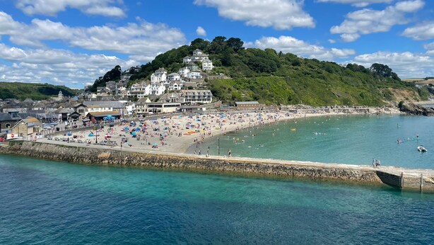 A coastal town with a beach, a pier, and buildings on a hill.
