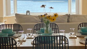 A dining area with a view of the sea, a sofa, and a table set with teal bowls and glasses.