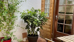 Eine Terrasse mit Holztür, einem Blumentopf, einem roten Topf und einem Holztisch mit Metallbeinen.
