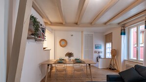 Ein Essbereich mit einem Holztisch, gedeckten Plätzen für vier Personen, klaren Stühlen, einer hängenden Pflanze und einem an der Wand befestigten Regal.