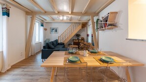 Ein Essbereich mit Holztisch, gedecktem für zwei Personen, klaren Stühlen und einer Treppe zu einem anderen Raum.