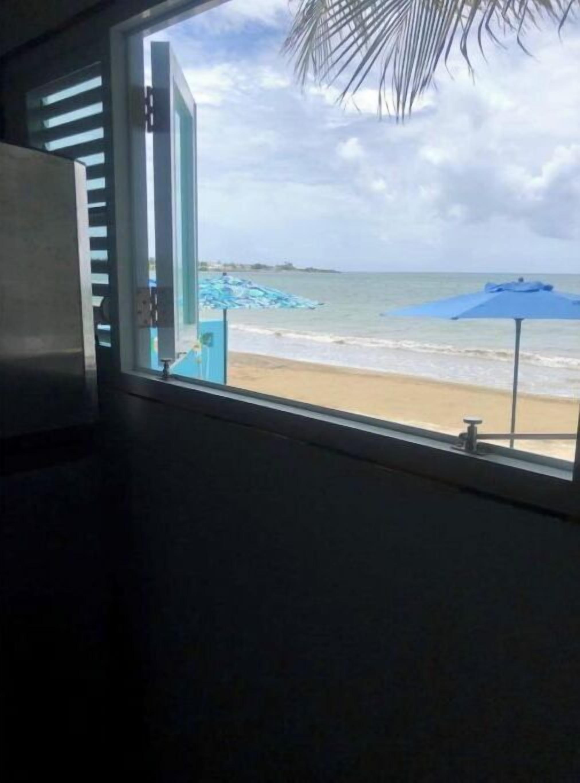 Blick aus dem Fenster auf einen Strand mit einem blauen Sonnenschirm.