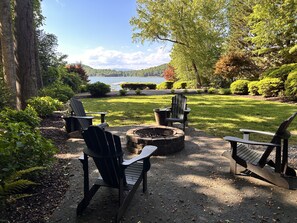 An outdoor seating area with Adirondack chairs, a fire pit, and a view of a lake.