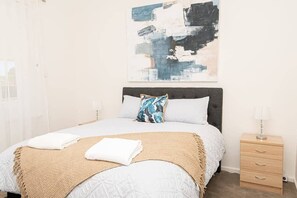 A bedroom with a bed, a nightstand, a lamp, and a painting on the wall.
