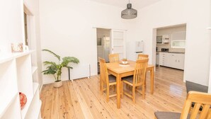 Ein Essbereich mit Holztisch und -stühlen, einer hängenden Leuchte, einem Blumentopf und einer Küche im Hintergrund.