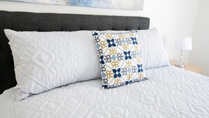 Ein Bett mit weißer gesteppter Tagesdecke und zwei Kissen, eines schlicht weiß, das andere mit einem geometrischen Muster.