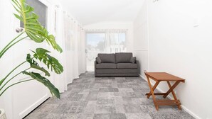 Ein schmales Entree mit grau gemustertem Boden, einem grauen Sofa, einem Holztisch und einer großen, grünen Pflanze.